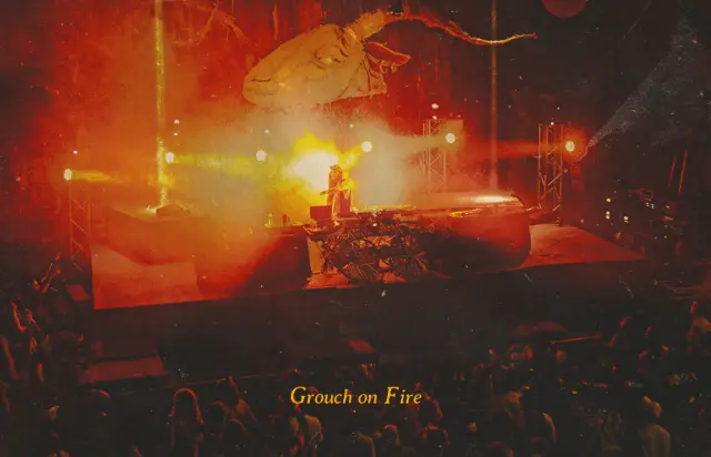 Grouch on fire. A DJ performing under red lights and haze.