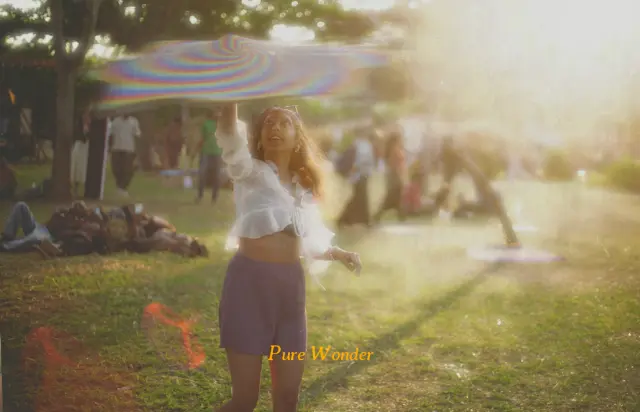 Pure wonder. A woman lifting shimmering fabric in the afternoon sun.