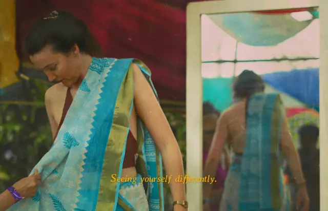 Seeing yourself differently. A woman trying on a blue sari in front of a mirror.
